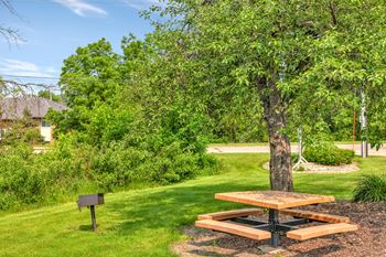 A picnic table sits in the middle of a grassy area with a tree nearby. at Windsor Crest Apartments, Davenport , IA, 52807